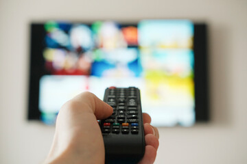 Tv remote controller in hand of customer looking for content in Smart Tv app. Watching streaming services on television.