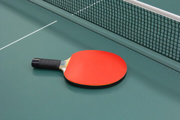 Red ping pong racket on the green table with net. Close up