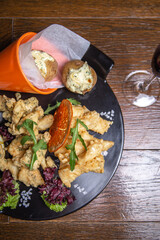 Delicious fried calamari, potatoes, and lemon wedges on a plate with red wine