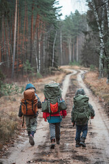 Boys and girl go hiking with backpacks on forest road bright sunny day