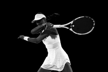 Tennis sportswoman in motion, about to strike shot to ball on court against black studio...