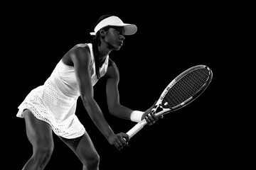 Focused, fit tennis sportswoman in ready stance against black studio background. Monochrome filter....