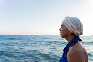 Beautiful woman with Greek attire on her head and dark blue sarong contemplating the Aegean Sea on a summer morning south of the Greek island of Crete