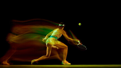 Dynamic photo of young woman preparing to hitting ball against black studio background in motion...