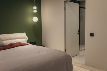 Bedroom with a bed, bedside table and lamps, with an olive wall and an entrance to the bathroom
