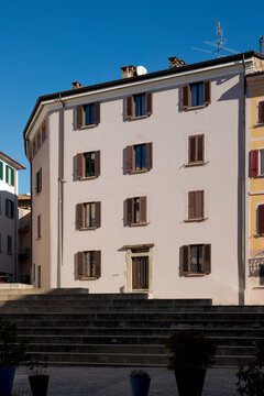 Old, recently renovated house in the center of a small town in Ticino, with many windows and shutters, some open, some closed.