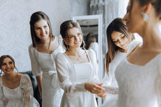 Bridesmaids rejoice in the morning, helping to fasten the buttons on the wedding dress and prepare for the wedding ceremony. They take pictures, smile, help the bride with her shoes.