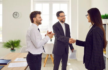 Group of a happy young three business people standing in the office making a good deal. Man shaking hands with woman reaching agreement or signing a contract or greeting new employee.