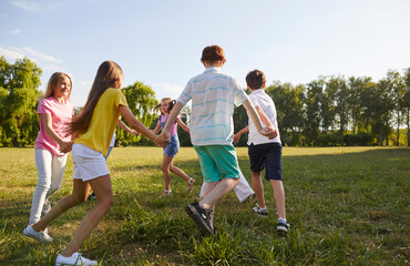 Happy, carefree children having fun during the summer break. Group of little friends dancing a round dance all together on green grass in the park on a good summer day