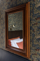 Vintage wooden mirror against a floral wallpaper.