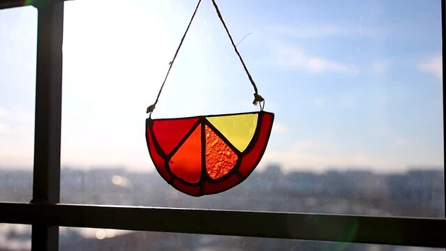Stained glass decor bright orange slice hanging on window against cityscape background