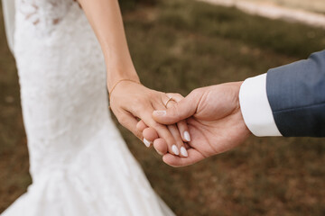 Close-up of bride and groom holding hands with wedding rings at reception outside in the backyard.
