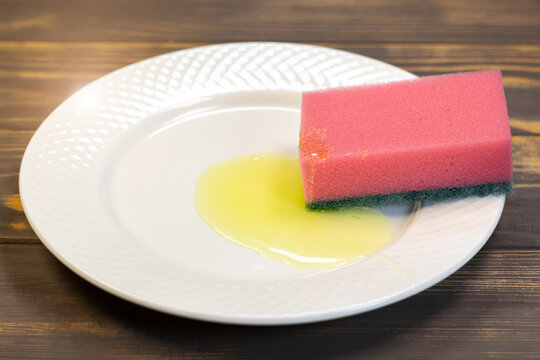 Red sponge for washing dishes on the white plate. Things for kitchen house cleaning.