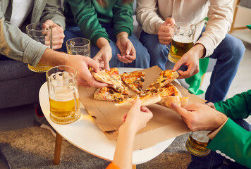 Crop group of male and female friends sitting around small table, eating pizza slices, drinking beer from big glass mugs, relaxing and having good time together. Party food concept - Powered by Adobe