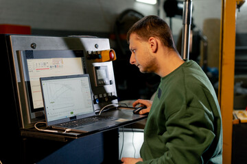 At a coffee roasting factory a worker in a green sweater turns on the roasting machine via laptop