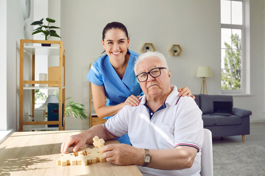 Elderly man with friendly caregiver solving puzzles as memory training against Alzheimer's and dementia. Portrait of senior man and young smiling nurse in modern specialized nursing home.
