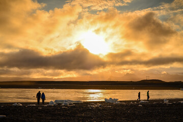 Fototapeta premium Silhouette of tourists enjoying the sunset amidst the remains of melted icebergs at the black beach near the Jokulsarlon glacial lagoon, Vatnajökull National Park, south coast of Iceland.