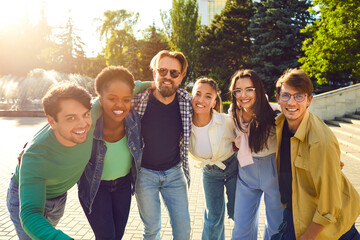 Portrait photo of multinational company of happy friends on walk on sunny summer day in city park. Attractive young people look into camera and smile. Concept of youth lifestyle and friendship.