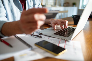 Cropped man holding a credit card using laptop at home