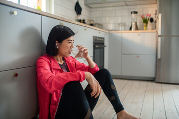 Sporty young woman drinking water on kitchen floor