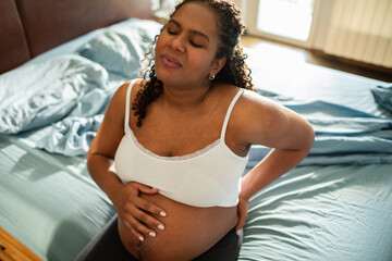 Pregnant African American woman with back pain holding her back in bedroom