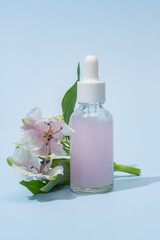 Serum with floral extracts for skincare. Nature cosmetics in glass bottle with pipette and pink alstromeria flowers on blue background. Face and body care spa concept.