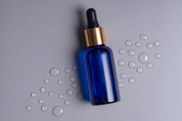 Blank blue glass essential oil bottle with pipette on gray background decorated waterdrops. Skin...
