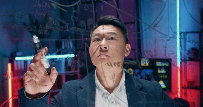 Portrait of asian businessman which writing important notes and attentively previsioning datas on the wall in the evening office