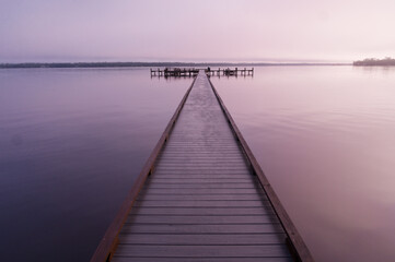 A wooden dock stretching far out into the still water of the St. Johns River on a foggy morning