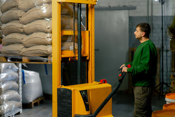 Fototapeta na wymiar a worker at coffee factory uses a yellow forklift to lower bags of coffee