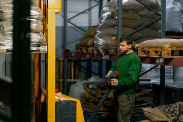 Fototapeta na wymiar A worker at coffee factory uses a yellow lifting fork to lift and insert forks into pallets