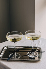 Two coupe glassed with sparkling wine decorated with satin ribbon bows standing on elegant silver tray