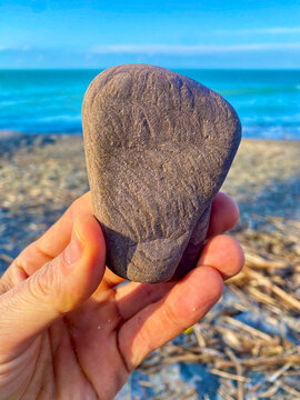 ancient stone tool artifact being held in a hand up to the sky against a lake beach backdrop