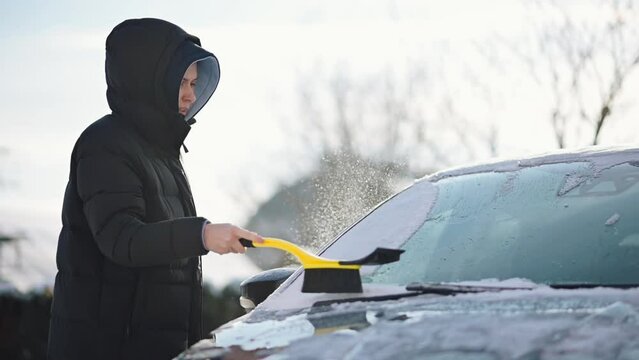 Girl Cleaning Car from Snow in Winter. Driver Brushing Snow off Car Windshield with a Brusher Scraper	