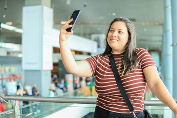 Selfie, young woman on the airport stairs, ready to travel, with a big happy smile. She uses her...
