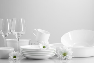 Fototapeta na wymiar Set of many clean dishware, flowers and glasses on light table