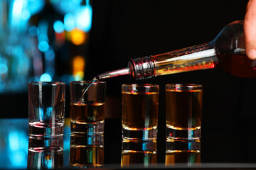 Pouring alcohol drink from bottle into shot glass at mirror bar counter, closeup