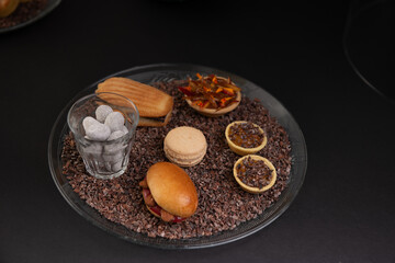 beautiful plate of cookies, macaron, Madeleine and chocolate placed on a black background