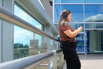 The woman chats on her smartphone on social media outdoors, just before entering the airport; she...