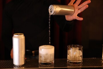 Bartender pouring energy drink into glass at counter in bar, closeup