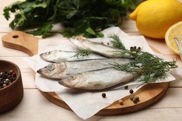 Fresh raw sprats, peppercorns and dill on light wooden table, closeup