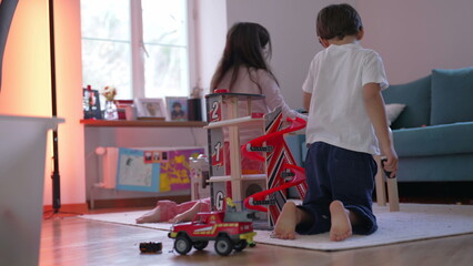 Obraz premium Little brother and sister playing in living room floor with toys, candid siblings interaction in imaginative creative play. Children leisure time