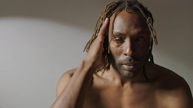 Portrait of a man with natural dreadlocks looking at the camera on a white backdrop