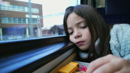 One bored little girl traveling by train plays with toy cars to pass the time struggling with boredom. Solo play of female 8 year old child with face leaning on window