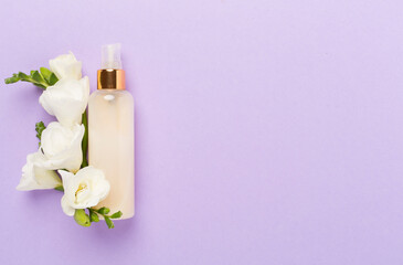 Cosmetic bottles with freesia flowers on color background, top view