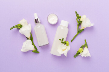 Facial cosmetic products with freesia flowers on color background, top view