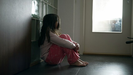 Sad child suffering from depression sitting alone in corridor feeling loneliness. Scared fearful...