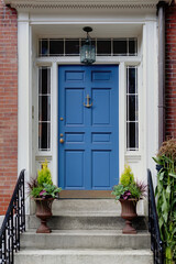 A vibrant blue front door features sidelight windows on each side and a transom window above. Two potted plants outside the door in New England. - obrazy, fototapety, plakaty
