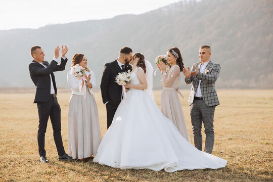 Wedding photo session in nature. The bride and groom kiss and their friends