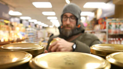 Close-up of many product jars with metallic lids in a grocery store and a male buyer chooses one